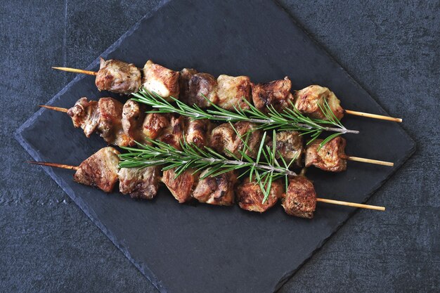 Juicy kebab with rosemary on a dark stone board.