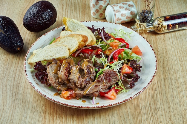 Juicy meat salad with baked veal vitello tonato, lettuce, onions and cherry tomatoes in a white bowl on a wooden table. Healthy food. Close up view