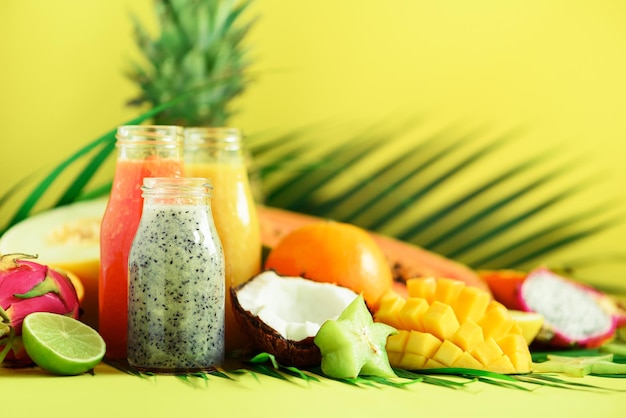 Juicy papaya and pineapple mango orange fruit smoothie in jars on yellow background Detox summer diet food vegan concept Copy space Fresh juice in glass bottles over palm leaves