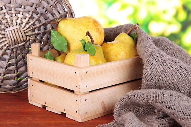 Juicy pears in wooden box on table on bright background