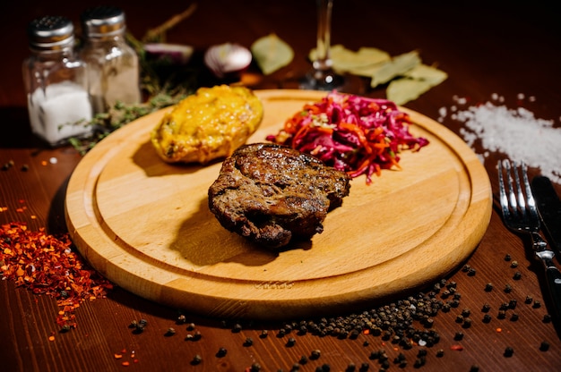 Photo a juicy piece of fried meat lies on a cutting board against a wooden table.top view