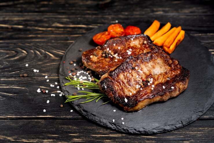Photo juicy piece of fried meat lies on a stone plate against a black wooden table
