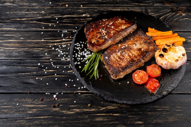 Juicy piece of fried meat lies on a stone plate against a black wooden table