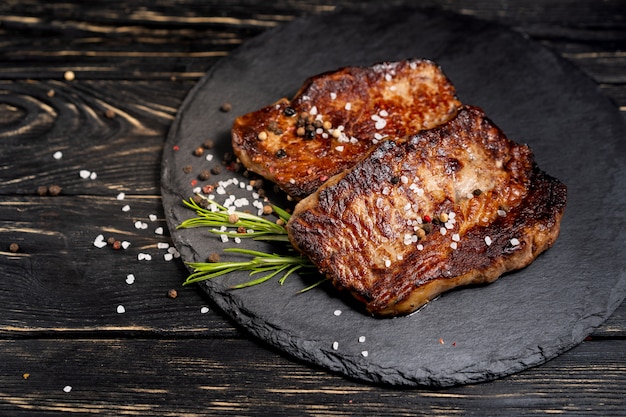 Juicy piece of fried meat lies on a stone plate against a black wooden table