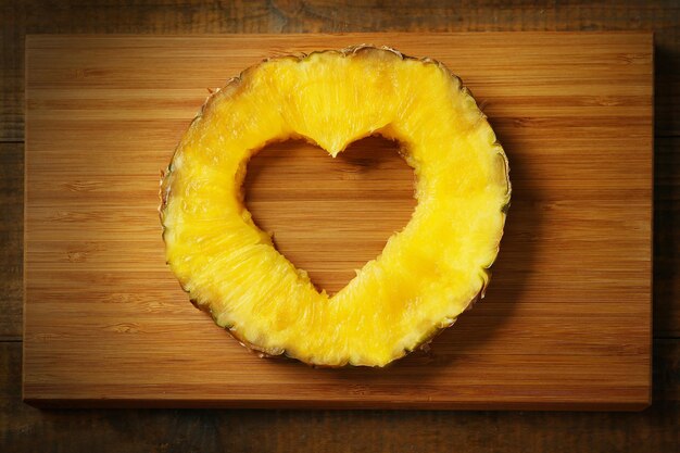 Juicy pineapple slice with cut out heart shape on wooden cutting board