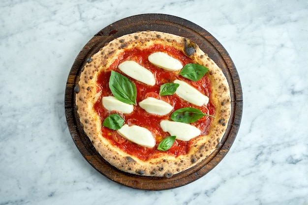 Juicy pizza margarita with red sauce, tomatoes, creamy\
mozzarella and basil. italian pizza from wood oven on wood board on\
marble table