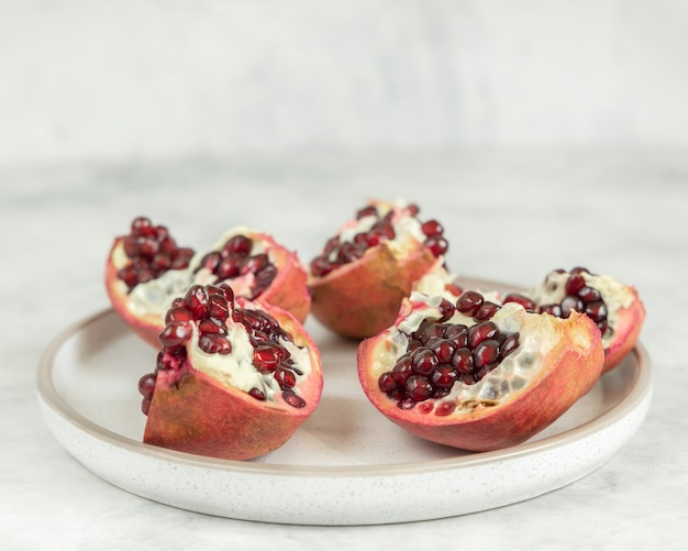 Juicy pomegranate pieces in plate on the white background, horizontal, selective focus