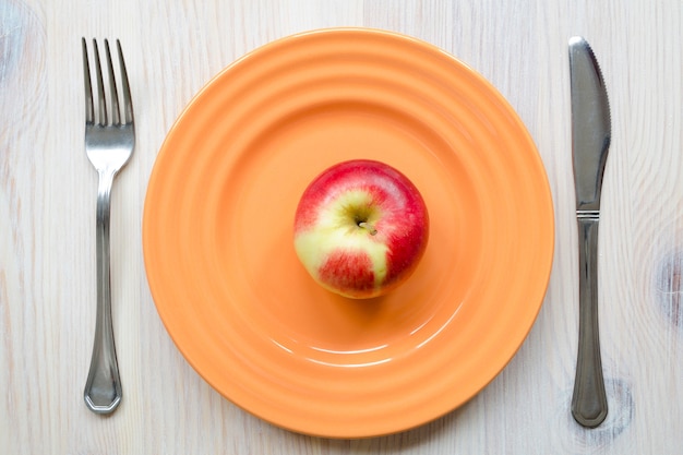 Juicy red apple on the orange plate with light wooden background