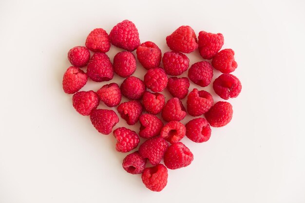 Juicy red heart made of organic fresh raspberries on white background