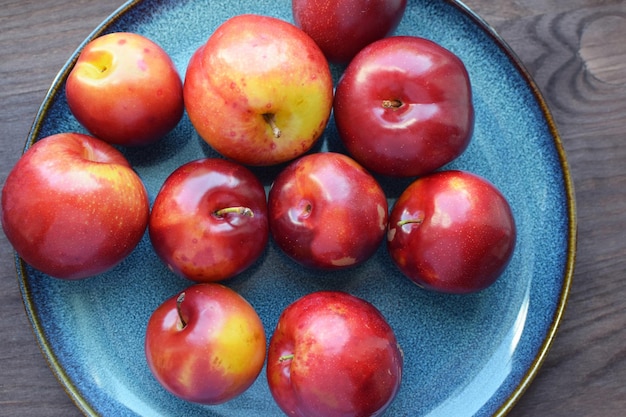 Фото Сочные красные спелые сливы на синей тарелке веганская концепция здоровые натуральные продукты