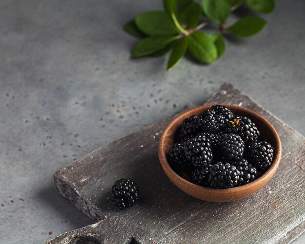 Juicy ripe blackberries on a wooden plate on a gray table