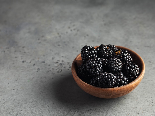 Juicy ripe blackberries on wooden plate on gray