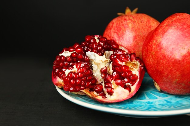 Juicy ripe pomegranates on wooden table, on dark background