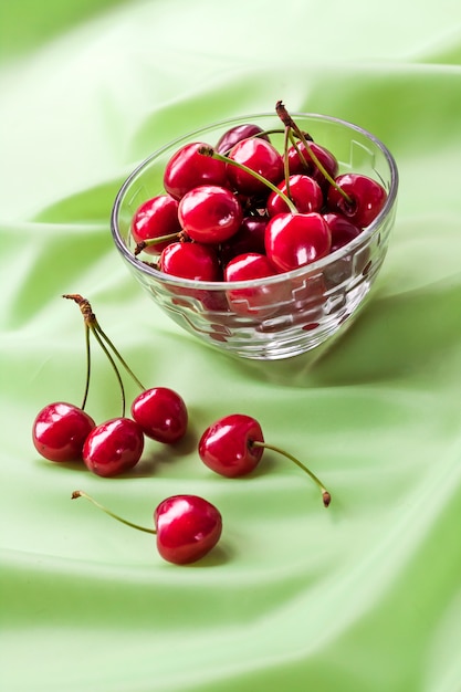 Juicy ripe sweet cherries in glass bowl on gently green cloth background