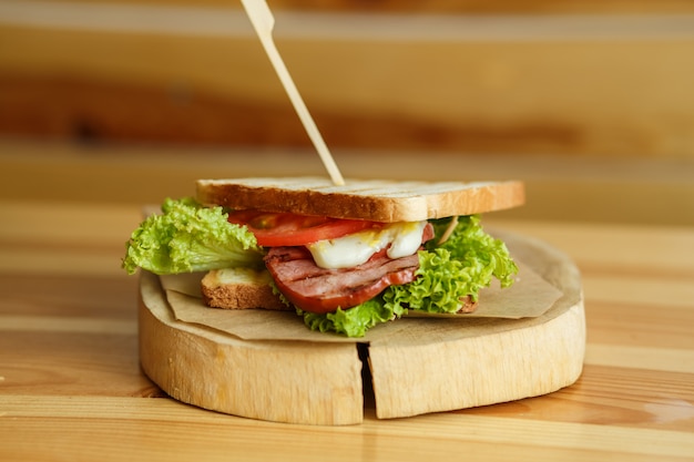 Foto panino succoso con pane grigliato e pancetta ti aspettano sul piatto di legno