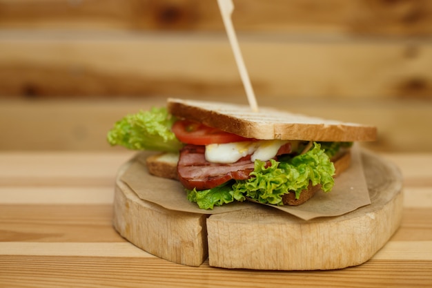 Juicy sandwich with grilled bread and bacon wait for you on wooden plate