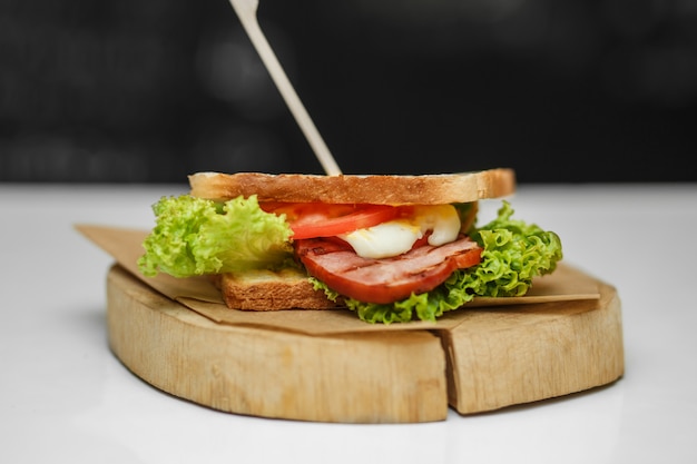 Juicy sandwich with grilled bread and bacon on wooden plate