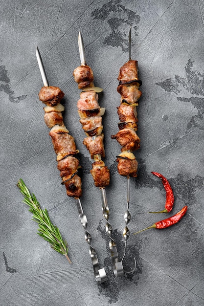 Spiedini succosi di carne di maiale o set di shashlik, su sfondo di tavolo in pietra grigia, vista dall'alto piatta