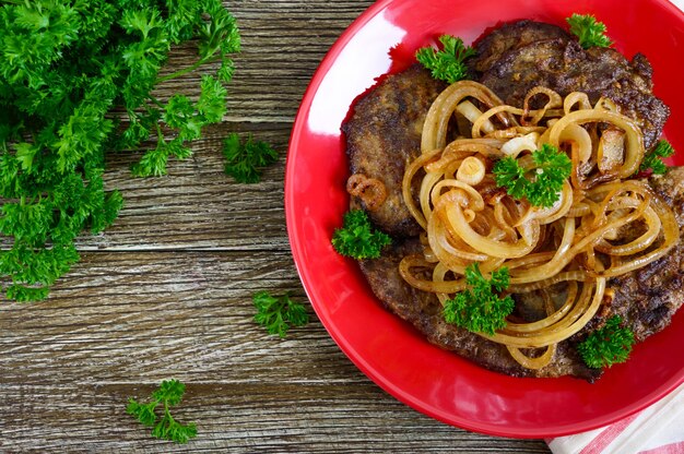 Сочные ломтики жареной печени и лука на красной тарелке. Вид сверху.