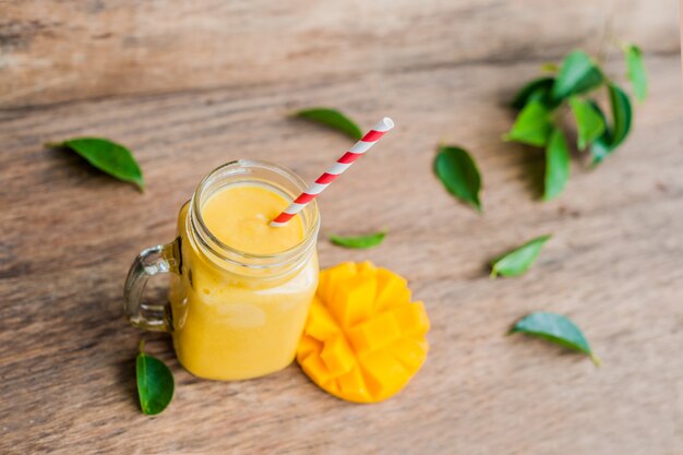 Juicy smoothie from mango in glass mason jar with striped red straw on old wooden background