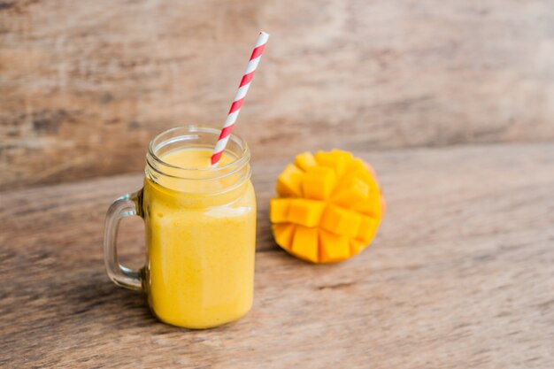 Juicy smoothie from mango in glass mason jar with striped red straw on old wooden background