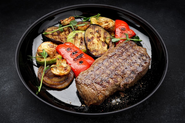 Juicy steak and grilled vegetables with spices on a plate on a dark background
