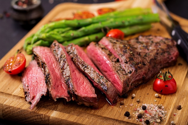 Juicy steak rare beef with spices on a wooden board and garnish of asparagus. 