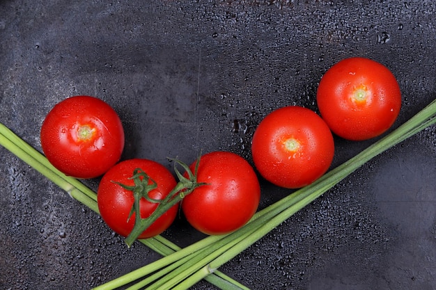 Juicy sweet red tomatoes and green sprigs on a black background Healthy food concept Closeup