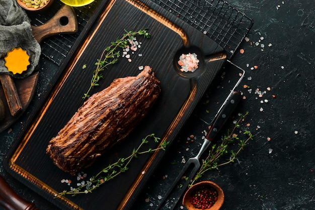 Juicy veal steak with spices on a black wooden board Top view Grilled meat