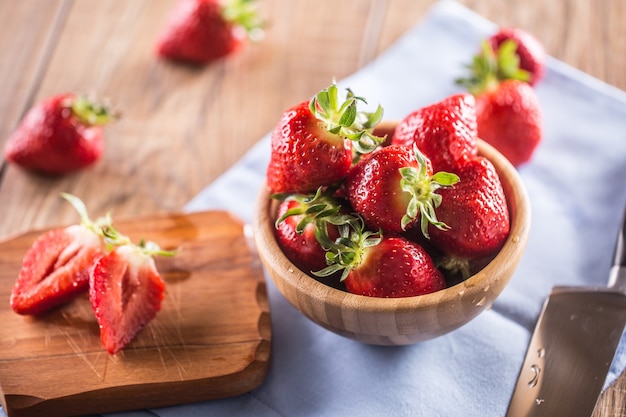 Juicy washed strawberries in wooden bowl on kitchen table.