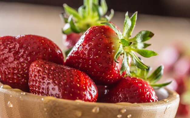 Juicy washed strawberries in wooden bowl on kitchen table.