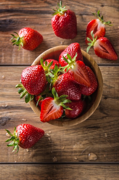 Juicy washed strawberries in wooden bowl on kitchen table.