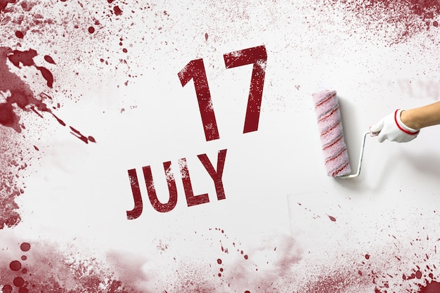 July 17th. day 17 of month, calendar date. the hand holds a
roller with red paint and writes a calendar date on a white
background. summer month, day of the year concept.