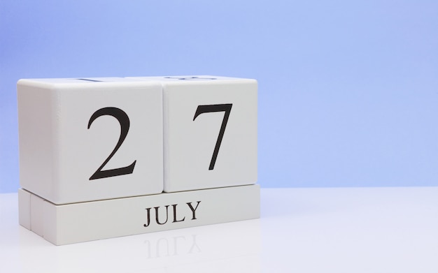 Photo july 27st. day 27 of month, daily calendar on white table with reflection, with light blue background.