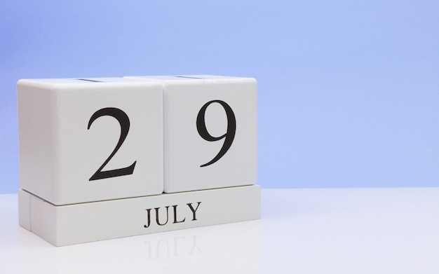 July 29st. Day 29 of month, daily calendar on white table with reflection, with light blue background. 