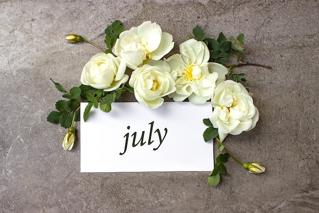 Июль. Месяц, календарный месяц. Белые розы граничат на пастельно-сером фоне с календарной датой. Лето, месяц года концепции.