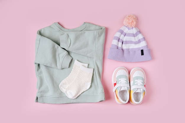 Foto maglione e cappello con scarpe da ginnastica. set di vestiti e accessori per bambini per la primavera, l'autunno o l'estate su sfondo rosa. vestito alla moda per bambini. disposizione piatta, vista dall'alto