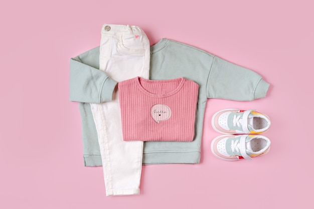 Jumpers  and pants with sneakers. Set of baby clothes and accessories for spring, autumn or summer on  pink background. Fashion kids outfit. Flat lay, top view