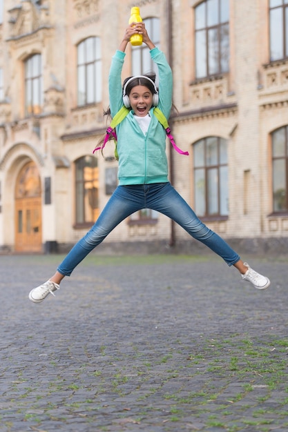 ジャンプする幸せな子供は、屋外のアクティブでエネルギッシュな子供時代のウォーターボトルで自由と喜びを感じます。