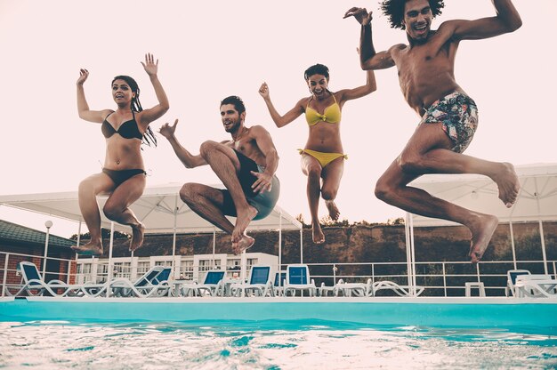 Прыгая в свежесть. Группа красивых молодых людей, выглядящих счастливыми, вместе прыгая в бассейн