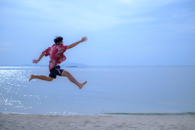 Jumping jonge man in het zand in de buurt van de zee