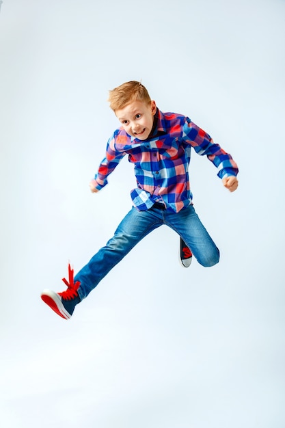 Jumping little boy in the colorful plaid shirt, blue jeans, gumshoes. Isolated.