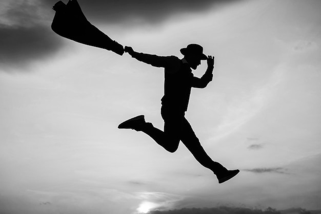 Силуэт прыгающего человека в шляпе и куртке танцует на фоне закатного неба бесплатно