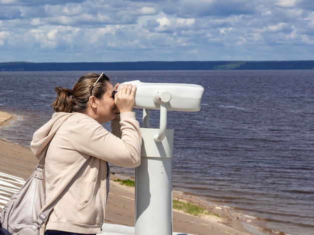 Il 19 giugno 2022 a cheboksary una donna guarda attraverso un telescopio binoculare i turisti sull'argine