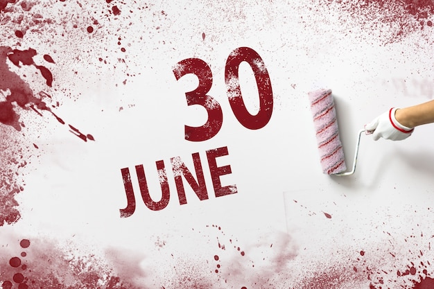 June 30th. day 30 of month, calendar date. the hand holds a\
roller with red paint and writes a calendar date on a white\
background. summer month, day of the year concept.