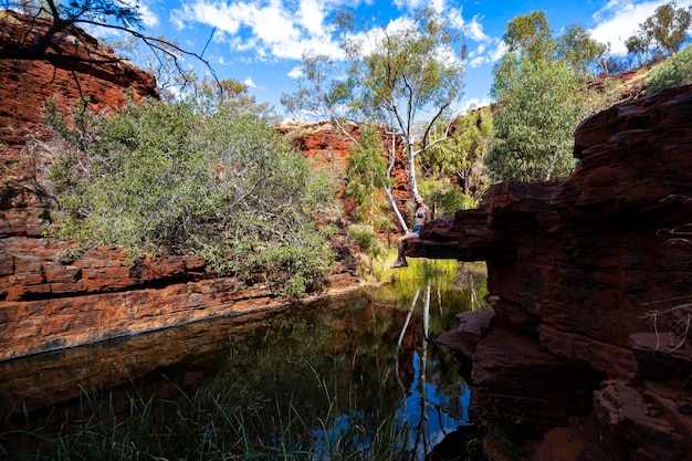 A jungle girl in a bikini sits on rocks by a stream in a canyon in karijini national park