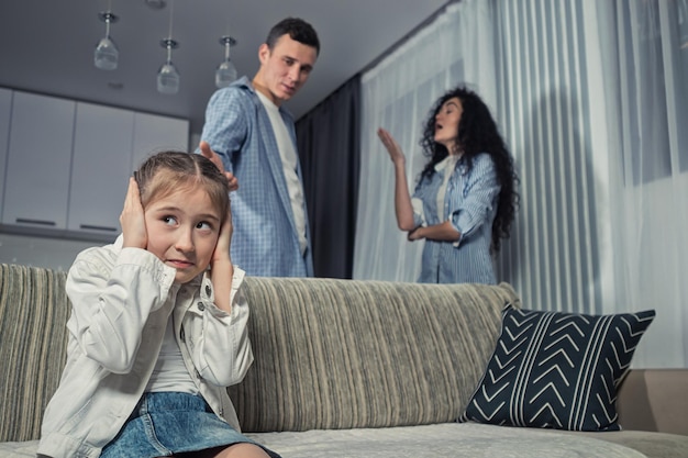 Junior schoolgirl sits closing ears against arguing parents