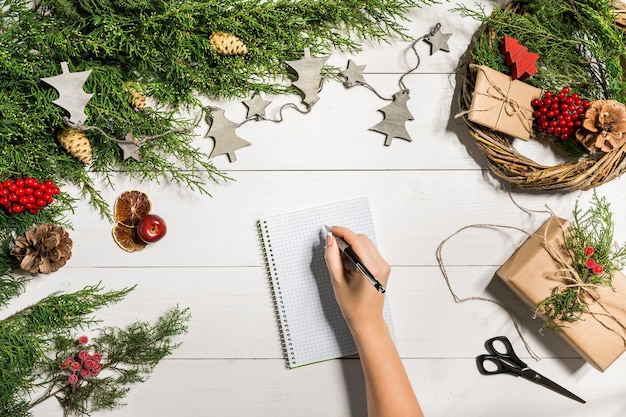 Juniper branches with a Christmas decor. Christmas, New Year background. Coniferous branches of juniper, notebook and a pen. Top view, flat design. Christmas tree on white wooden background.