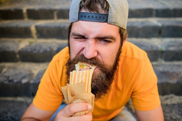 Junk food. Guy eating hot dog. Snack for good mood. Unleashed appetite. Street food concept. Man bearded eat tasty sausage. Urban lifestyle nutrition. Carefree hipster eat junk food while sit stairs.