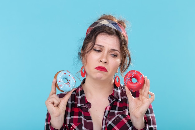 Junkfood, dieet en ongezonde levensstijl concept - pin-up vrouw met donuts over de blauwe achtergrond.